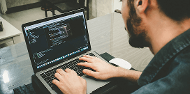 Developer writing and reviewing code on a laptop at a desk in an office setting.