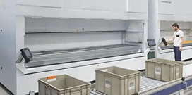 A worker uses a Modula LIFT system in front of a conveyor system moving plastic bins