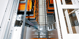 A close-up image of an orange and white Modula brand vertical lift system in a warehouse facility
