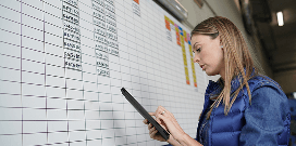 Employee using a tablet to update information on a warehouse scheduling or inventory board.